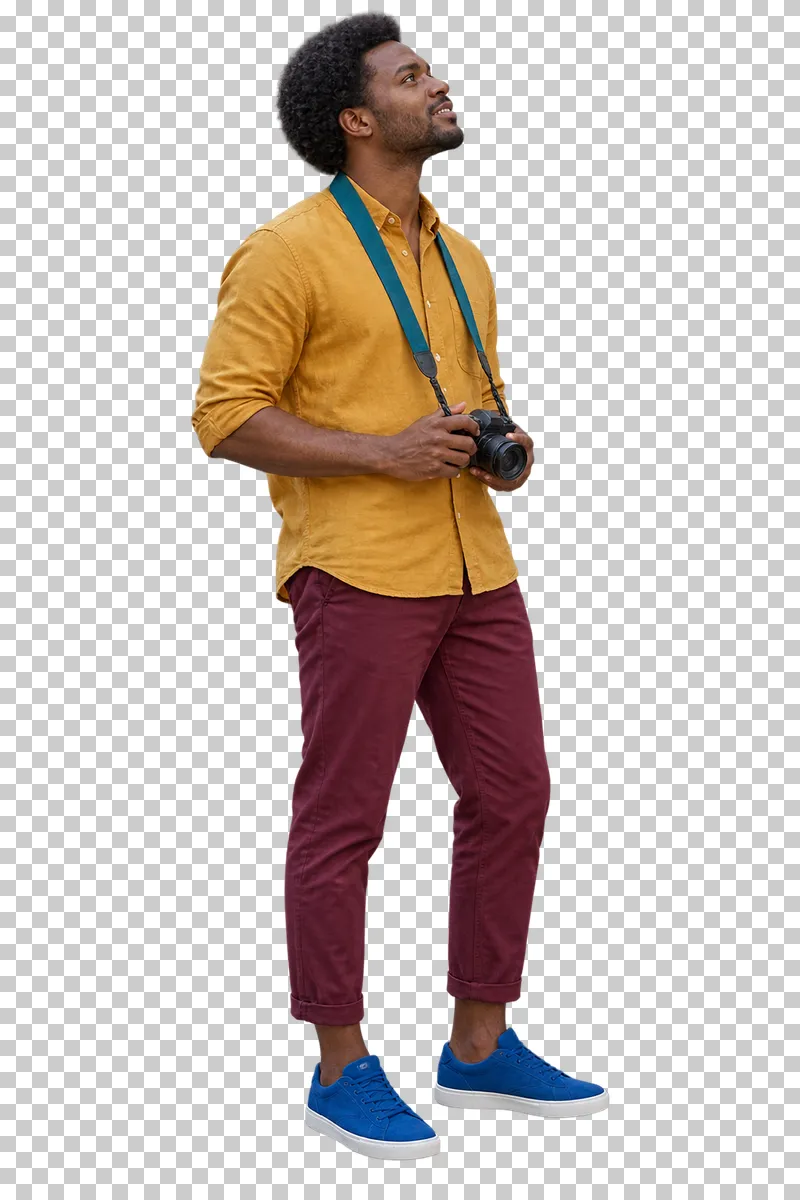 A man in a turmeric shirt and burgundy trousers holding a camera at his waist on a teal neck strap.