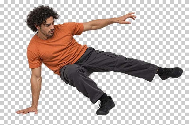 Male breaking dancer in an orange T-shirt and charcoal trousers extending one leg in a low kick-out.