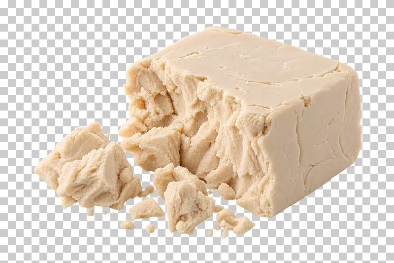 A pale fresh yeast block with a broken edge and crumbs.