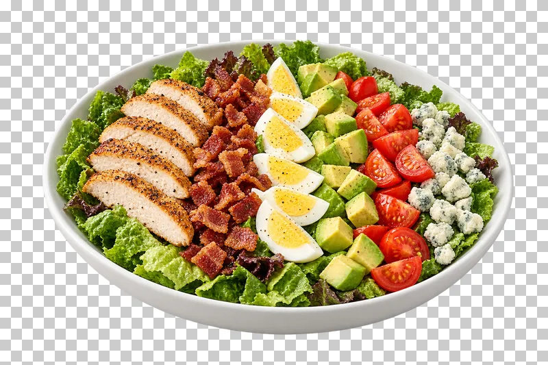 A white oval dish of Cobb salad with rows of chicken, bacon, egg, avocado, tomato and blue cheese.