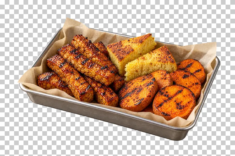 A parchment-lined metal tray of glazed tempeh, cornbread wedges and grilled sweet-potato rounds.