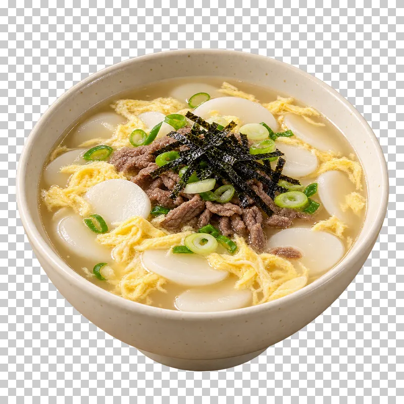 Tteokguk soup with oval rice-cake slices, egg ribbons, beef and seaweed in pale broth in an ivory bowl.